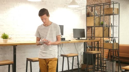 Casual Young Man Using Tablet While Walking in Office