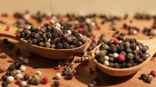 Dropping Colorful Whole Peppercorns into Two Wooden Spoons