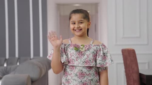 Happy Indian kid girl greeting to the camera by waving Hello