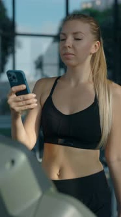 Portrait of Woman Scrolling Social Media on Phone Walking on Treadmill in Gym
