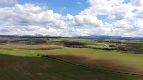 Aerial of Green fields with blue cloudy sky and snow-capped mountains in the distance