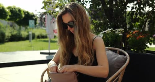 Mujer con cabello suelto busca cosméticos en un bolso de diseñador