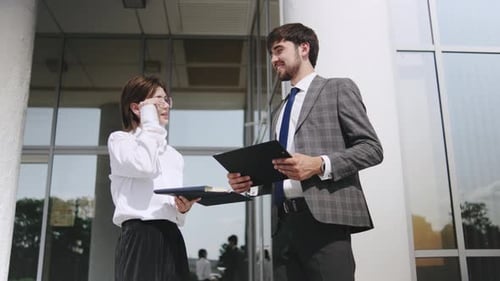 Business Professionals Discuss Project Plans Outside a Modern Office Building During a Sunny Day