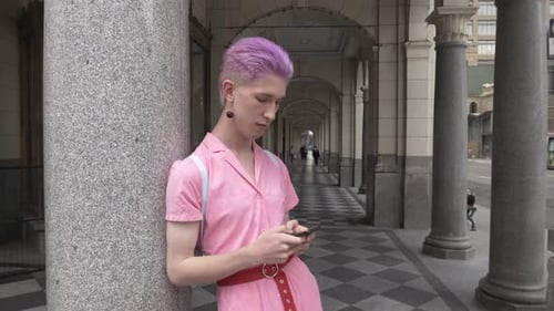 Stylish nonbinary young adult sings to smart phone on city sidewalk medium shot