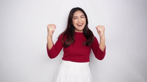 A young Asian woman with a happy successful expression wearing red top isolated by white background