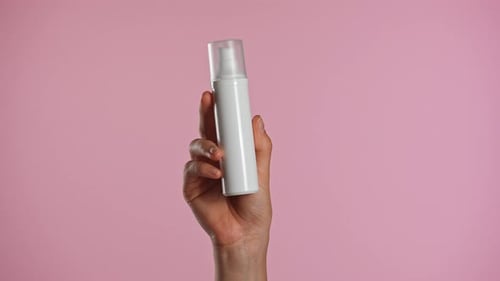 Hand Dispensing Beauty Product Against Pink Background