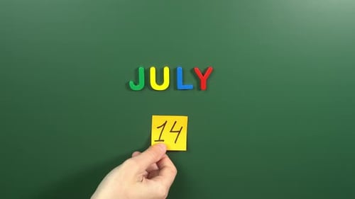 Hand sticking a sticker 14 July calendar day on school board. 14 date of July. Fourteenth day