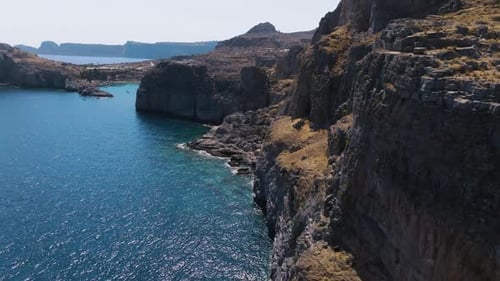 Aerial view flying close to rocky cliffs on the coastline of Rhodes, sunny Greece