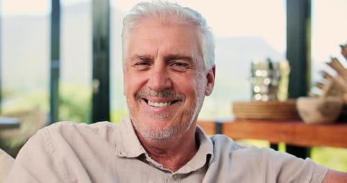 Happy, face and old man in lounge, relax and comfortable on couch, chill and laugh on break