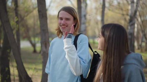 Male and Female Students Walking in Park Smiling and Sharing Jokes Sunlight Through Trees Casual