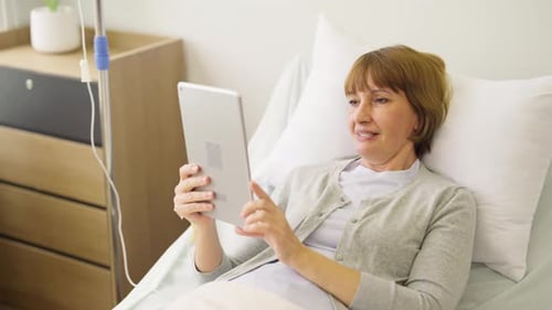 Close up senior woman patient lie on bed and enjoy to use tablet in patient room during relax