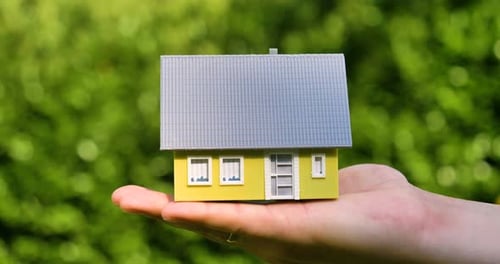 Hand Holding Miniature Home Against Green Background