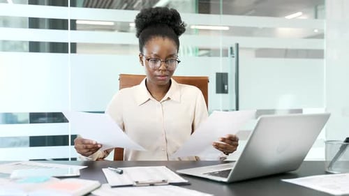 Empresaria afroamericana confundida que tiene dificultades con el papeleo sentada en la oficina de negocios