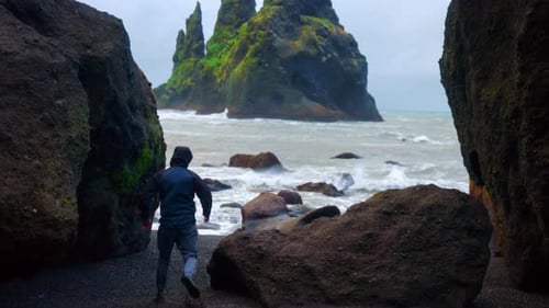Tourist Guy Running Towards The Coastal Rock Boulders At Reynisfjara Black Sand Beach, South Iceland