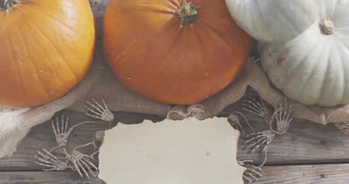 Paper with copy space against skeleton hands and pumpkins on wooden surface