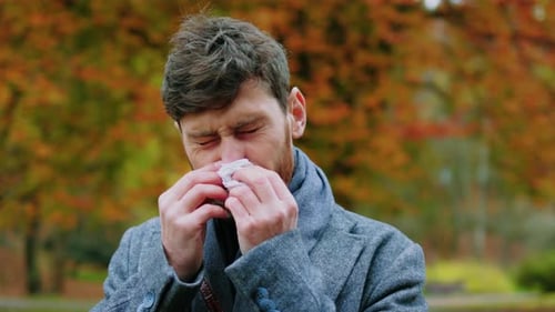 Man with Cold Blows Nose in Autumn Park
