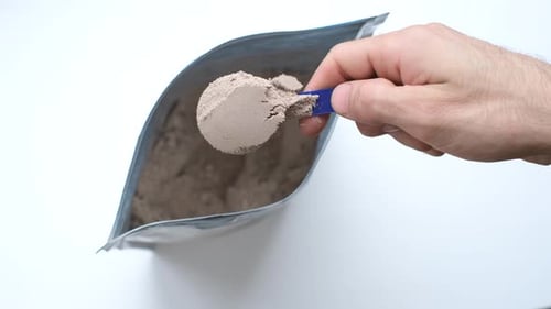 Male hand takes out a protein powder from a bag on white background top view.