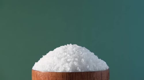 White Table Salt Granules Falling Into a Pile Wood Bowl Green Color Studio Background Condiment