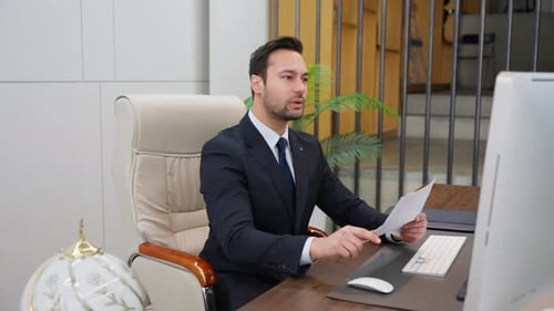 Businessman working with computer, holding business documents reading reports checking info office