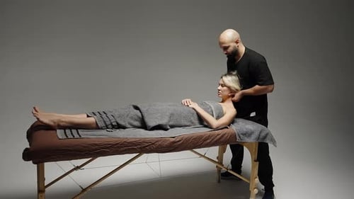 Professioneller Massagetherapeut, der eine entspannende Nacken- und Schulterbehandlung an einem liegenden Klienten durchführt
