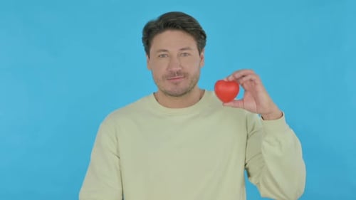 Man Holds Red Heart Against Blue Backdrop