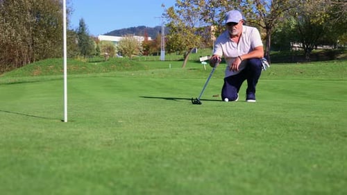 Focused senior golfer measuring with the putter on green for precise shot