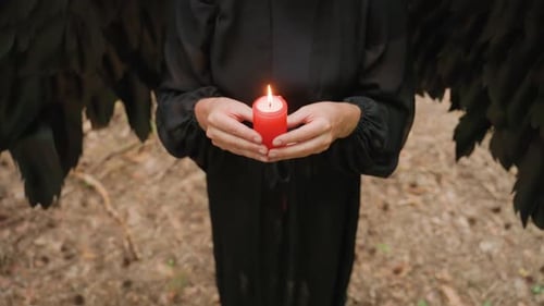 Person in Black Holding Burning Red Candle During Dark Forest Ritual