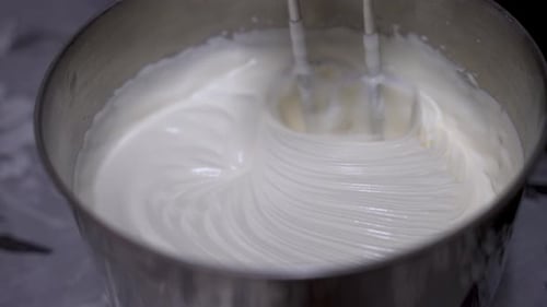Cream Being Whisked In Metal Tin By Machine On Kitchen Table. Slow Motion. Close Up
