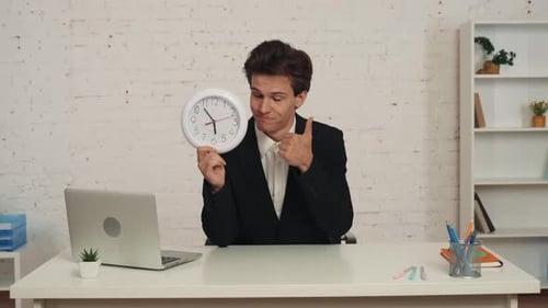 Medium Video of a Young Man Sitting at the Table in the Office Holding a Clock in His Hand Giving a