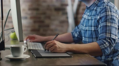 Young designer sitting in front of a monitor in a loft and sketching on a graphic tablet.