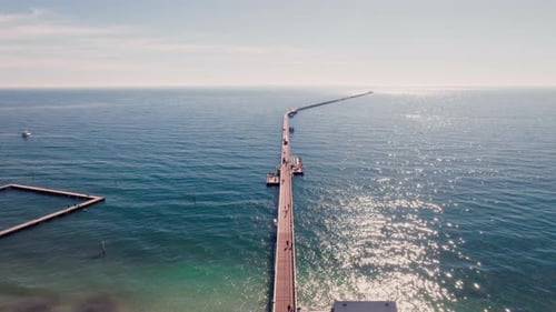 A long wooden pier extends far out into the ocean on a sunny day.