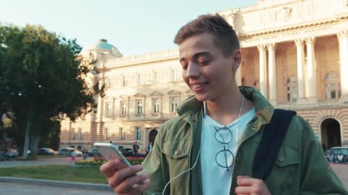 Handsome Young Man Use Phone Speak on Mobile in Headphone Look Around Walk Standing on Street City