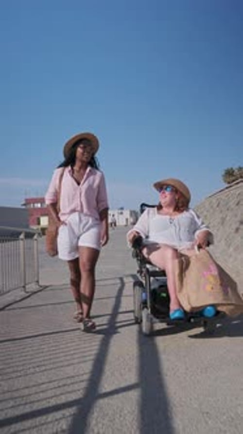 Woman Pushing Friend in Wheelchair on Promenade in Slow Motion