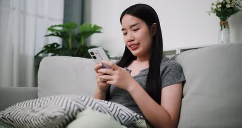 Woman Relaxing on Sofa Using Smartphone at Home