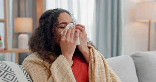 Allergies, sinus and sick woman sneezing on a sofa with tissue paper for nasal