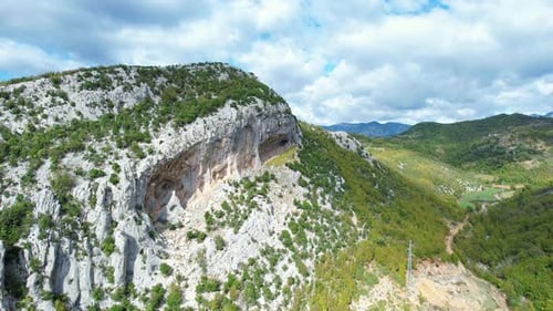 Aerial shot (smooth revealing an imposing rock cliff over a mountainous valley with a small