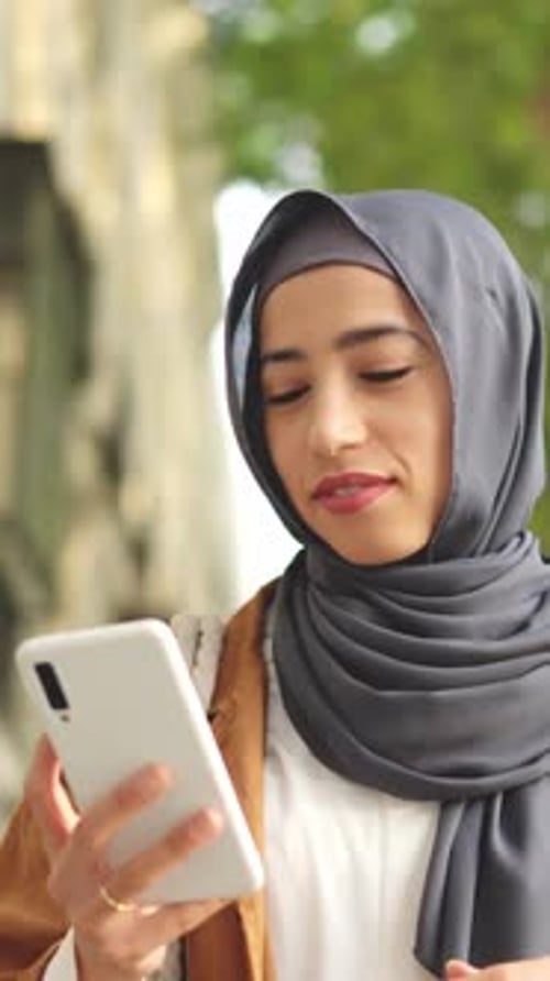 Happy Muslim Woman Walking While Using a Mobile in the Street