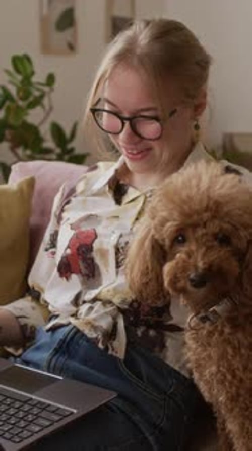 Vertical d'une fille heureuse passant un appel à l'aide d'un ordinateur portable et caressant un mignon mini-caniche