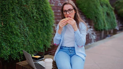 Frau beim Mittagessen mit einem Sandwich und Kaffee im Park mit einem Laptop