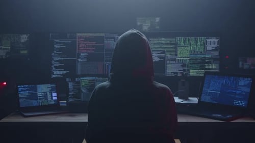 Hooded Figure Coding in Front of Monitors