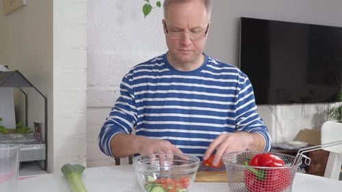 Middleaged Man Prepares a Fresh Mediterranean Salad in a Bright Kitchen