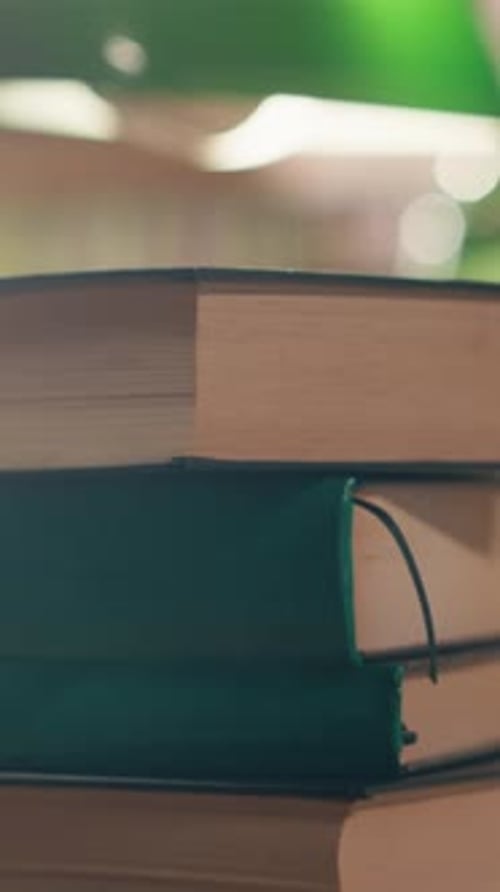 Vertical Video Stack of Books on Desk in Quiet University Library with Warm Lighting