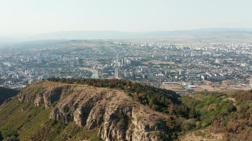 Aerial opening view of city of Tbilisi in Georgia appearing behind a mountain. Establishing shot, fo