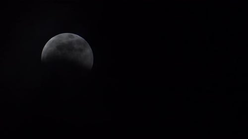 Thin clouds slowly reveal a full moon during a lunar eclipse. Moon on left side of frame.