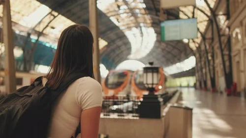 Woman traveler looks at the train traffic table at the railway station