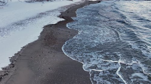 Winter Beach Landscape With Snow and Waves Under a Cloudy Sky in the Late Afternoon