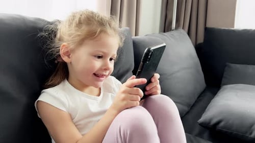 Smiling Girl Using Smartphone on Gray Couch