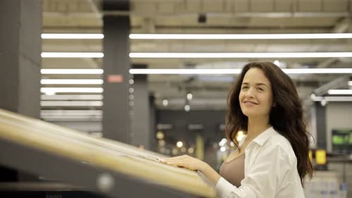 Smiling Young Woman Choosing Wooden Laminate Flooring in Store