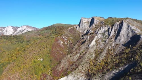 Flying above sunny autumn alpine mountain cliffs and colorful forest by drone