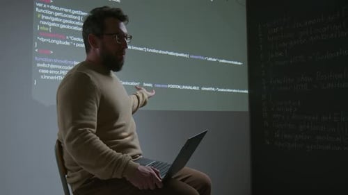 Caucasian Male IT Teacher Explaining Code Projected on Wall at Lecture